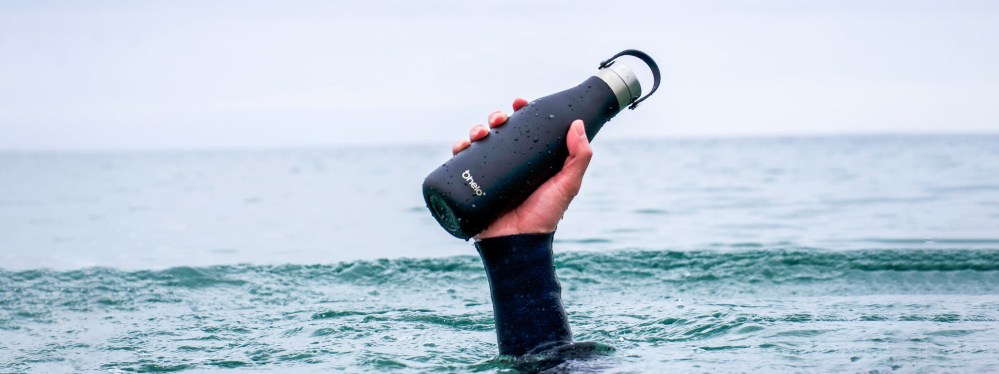 Ohelo insulated water bottle in hand coming out of the ocean