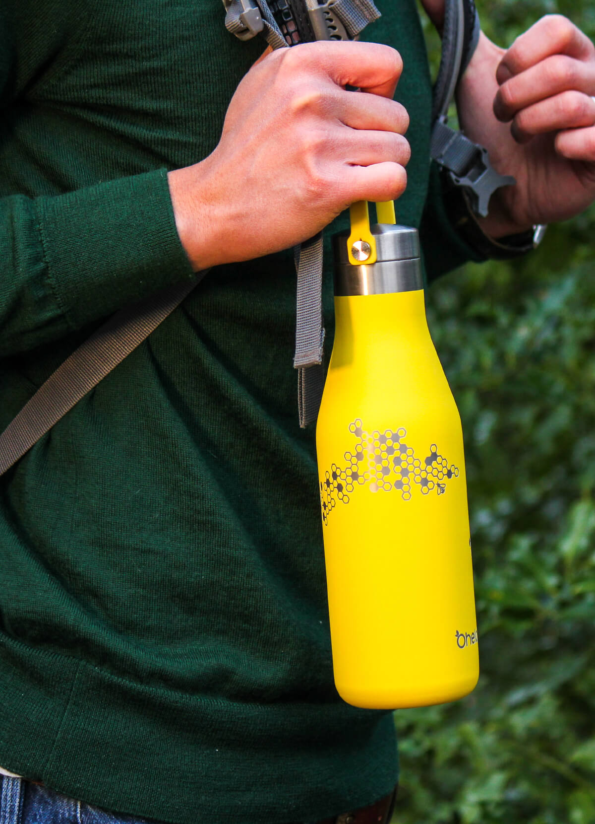 Man in green jumper with backpack hiking holding an Ohelo yellow bee insulated water bottle by the carry strap