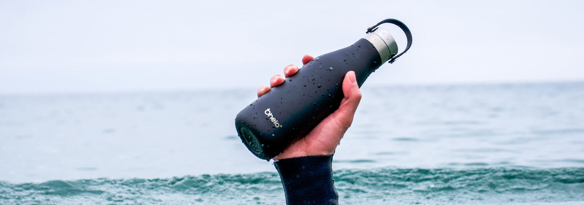 500ml black ohelo reusable water bottle being held by hand coming out of the ocean